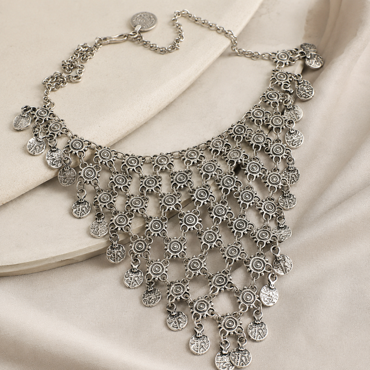 Angled view of a silver-tone coin dangle necklace with layered charm strands.