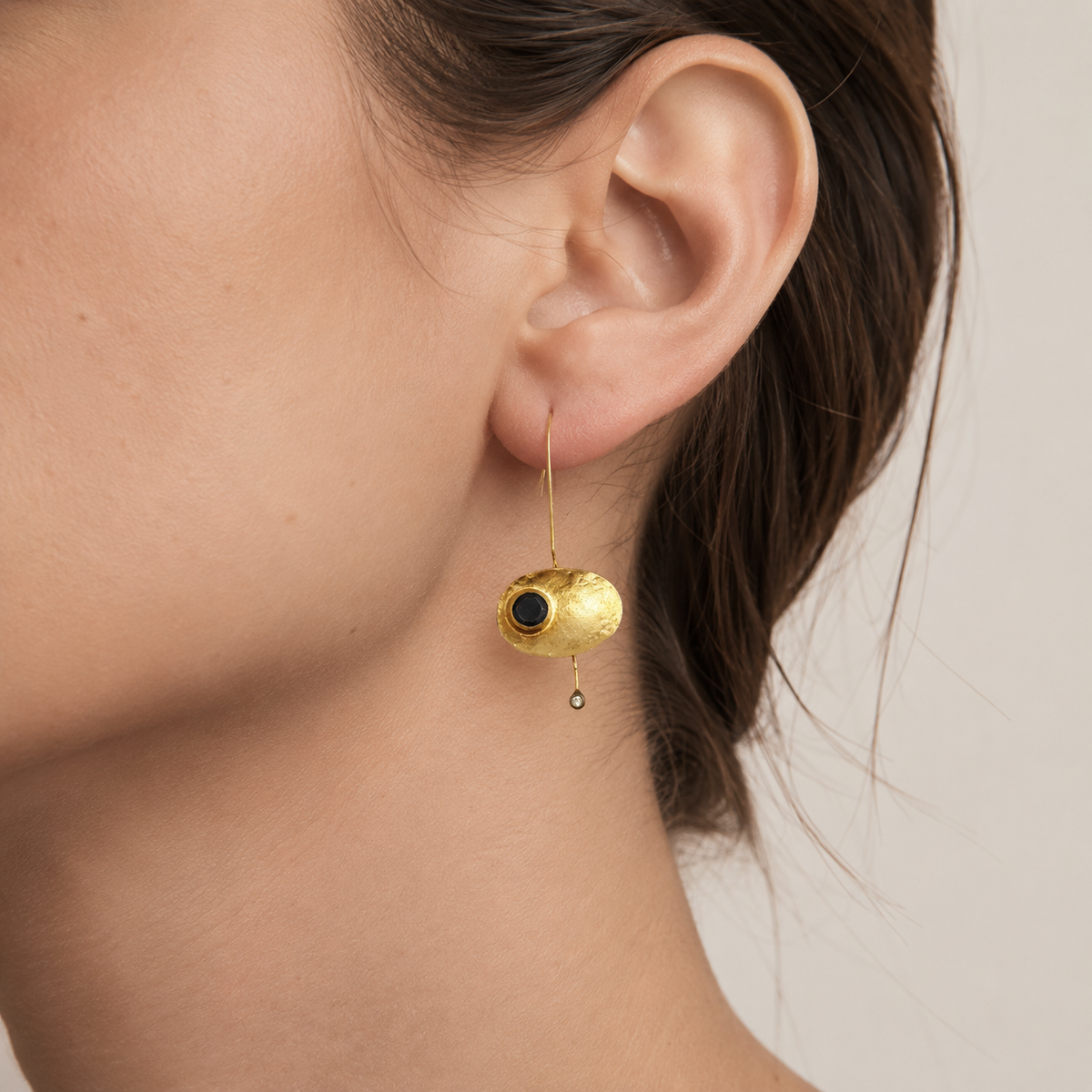Pair of oval gold-plated earrings with black stone centers and a delicate drop detail.