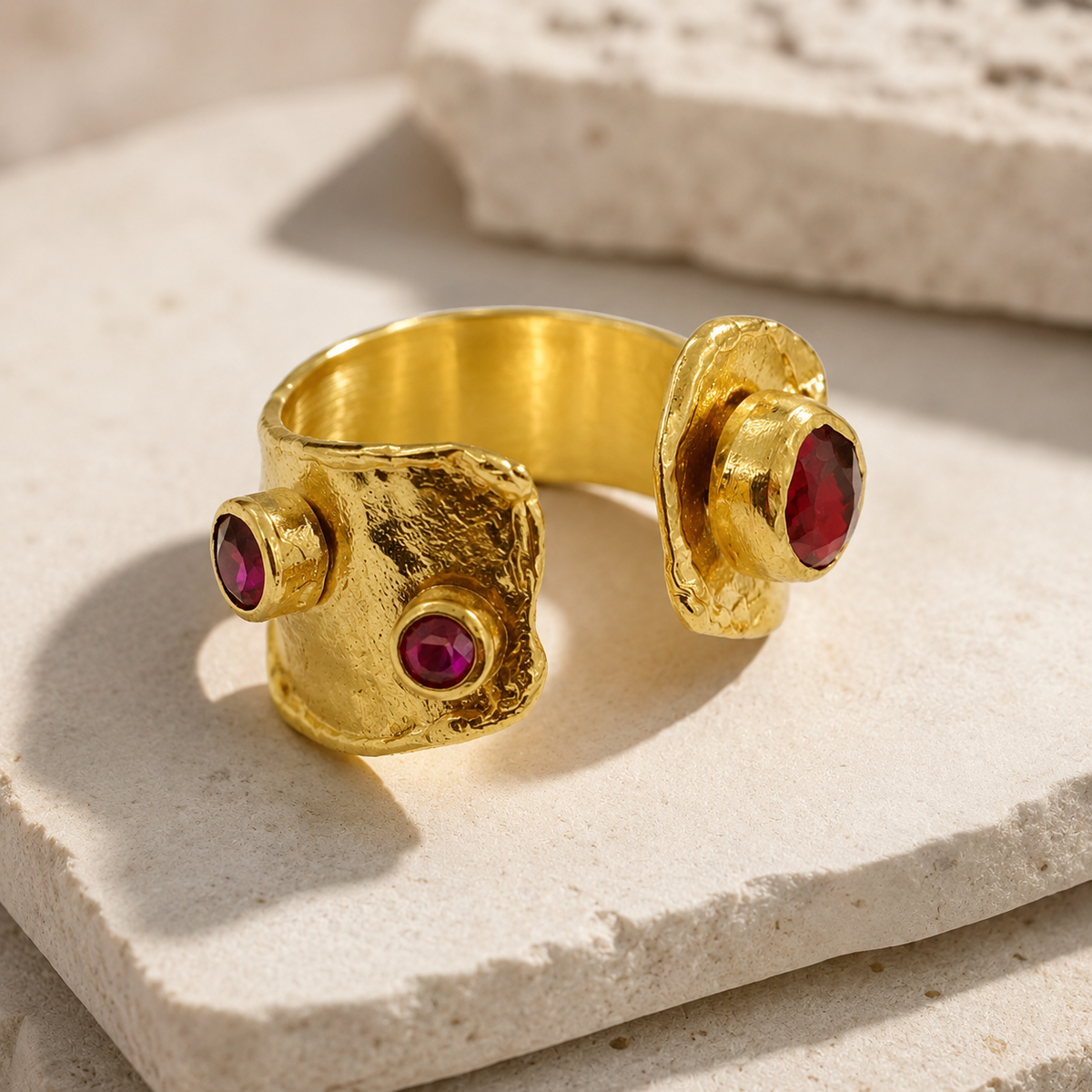 Side angle of a gold-plated open cuff ring with garnet red stone details.