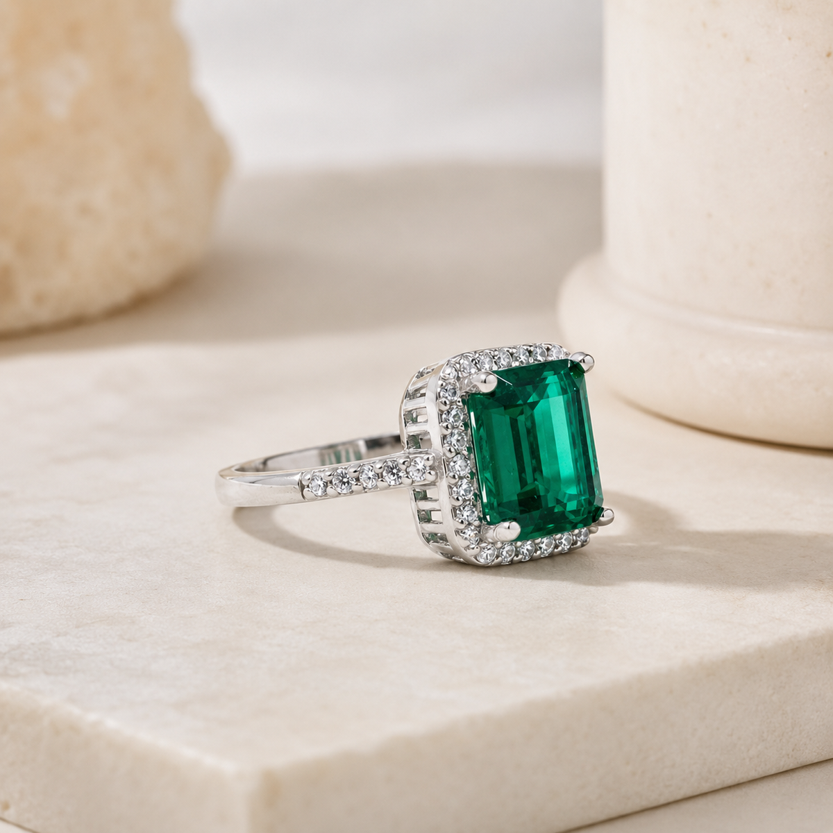 Side angle of a silver-tone ring with an emerald-cut green stone.