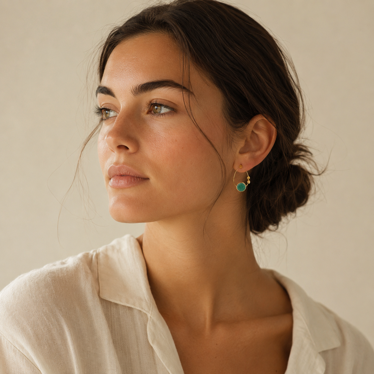 Gold-plated hoop earrings with round green stones in a simple studio view.