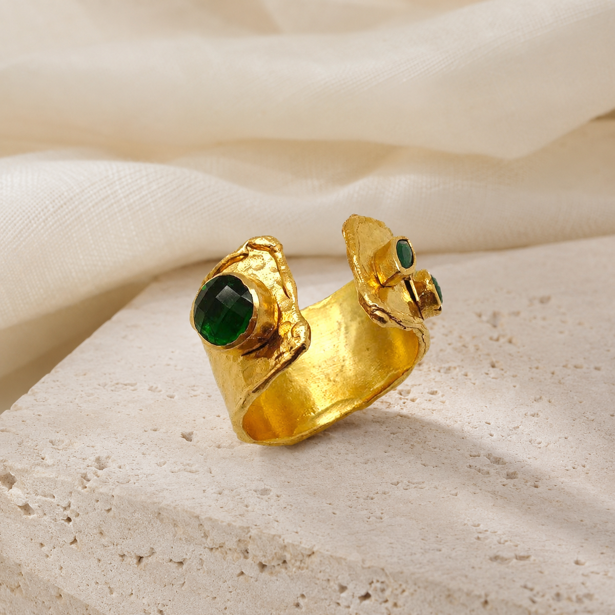 Gold-plated open cuff ring with emerald green accents on a white background.