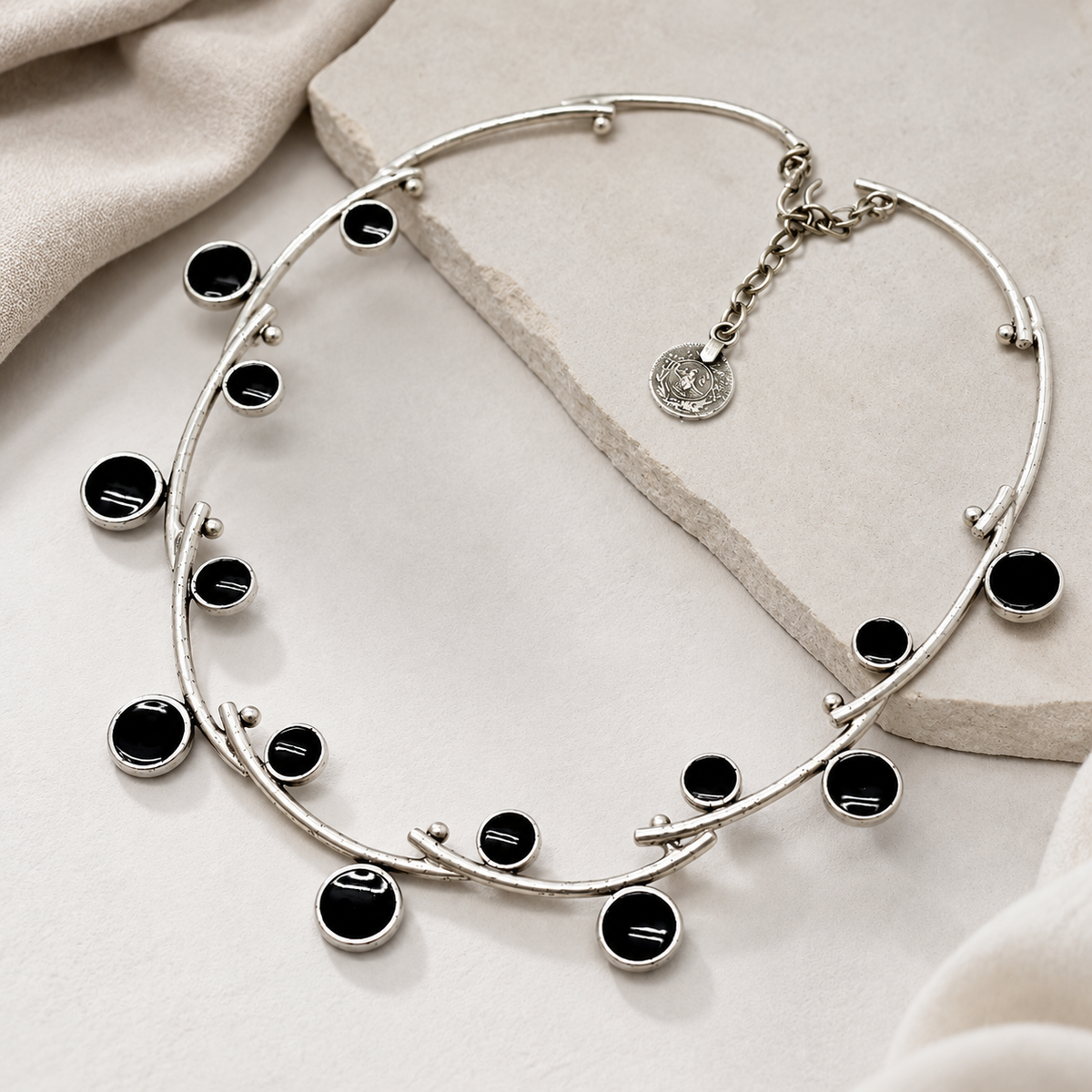 Angled view of a silver-tone open wire collar necklace with glossy black stone accents.