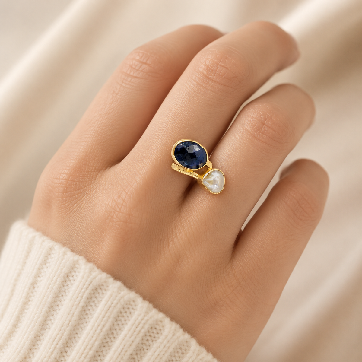 Gold-plated two-stone ring with navy blue and white stones on a white background.