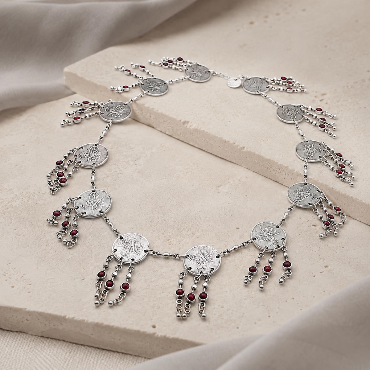 Angled view of a silver-tone coin fringe necklace with red bead details.