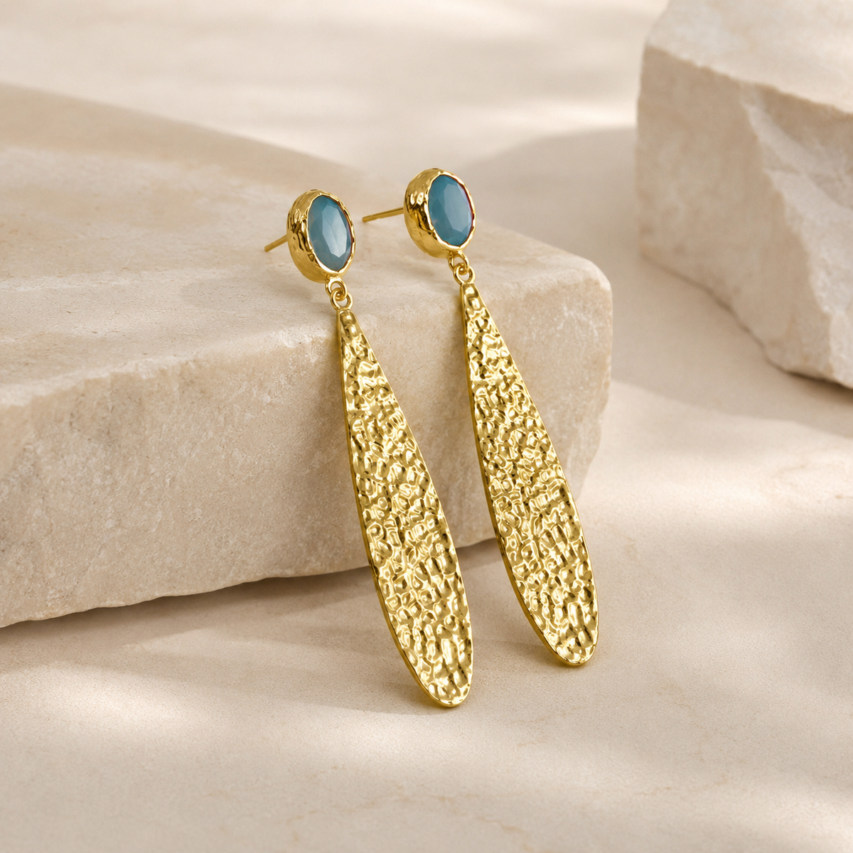 Side view of hammered gold-plated drop earrings with textured long drops and blue oval tops.