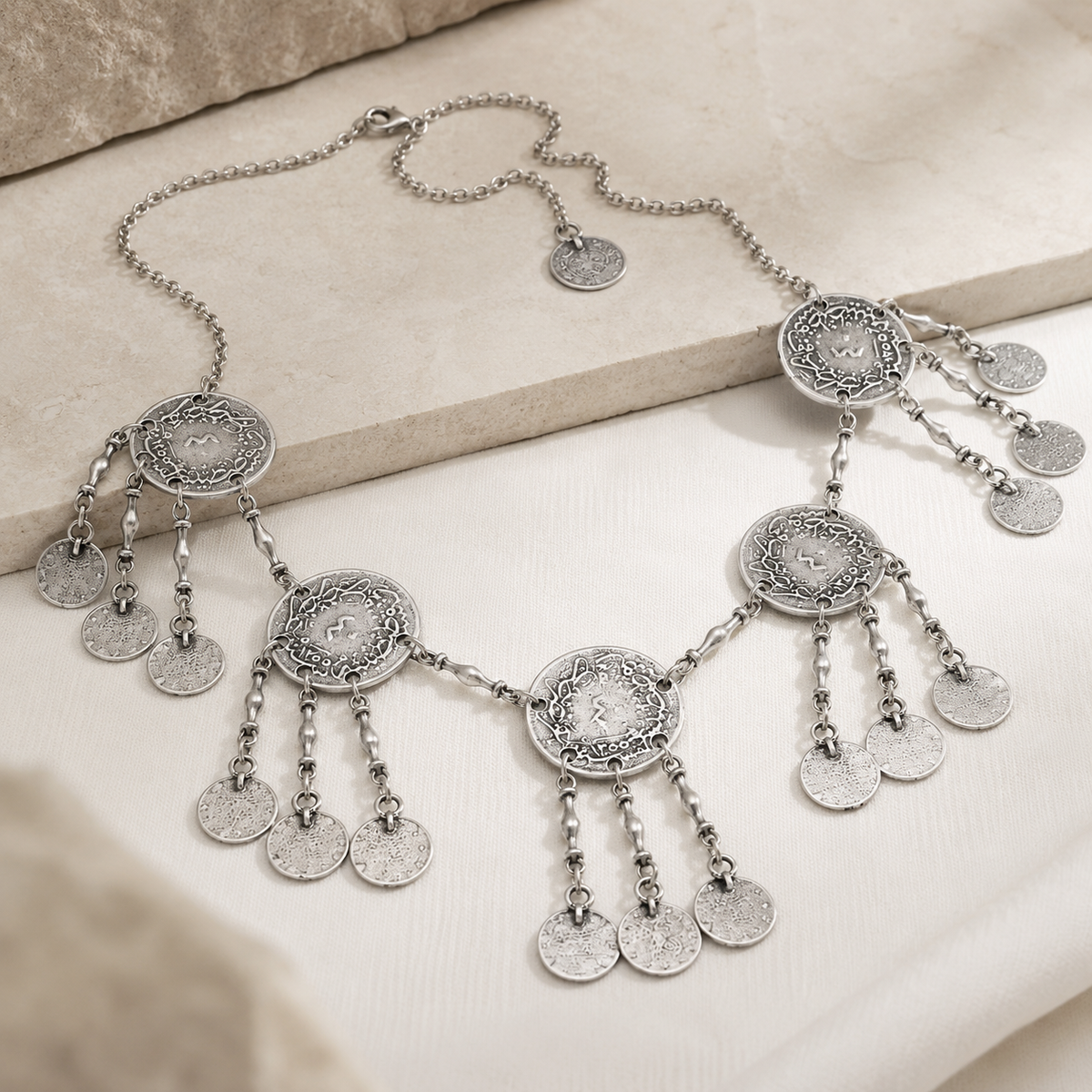 Angled view of a silver round coin fringe necklace with layered charm details.