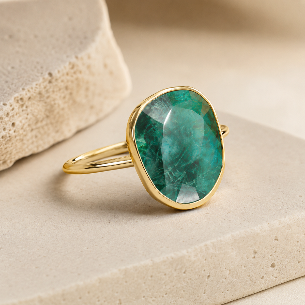 Side angle view of an emerald green oval gold-plated ring.
