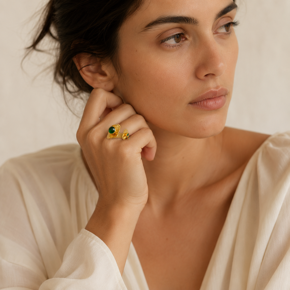 Gold-plated ring with emerald green stone details and an open cuff silhouette.