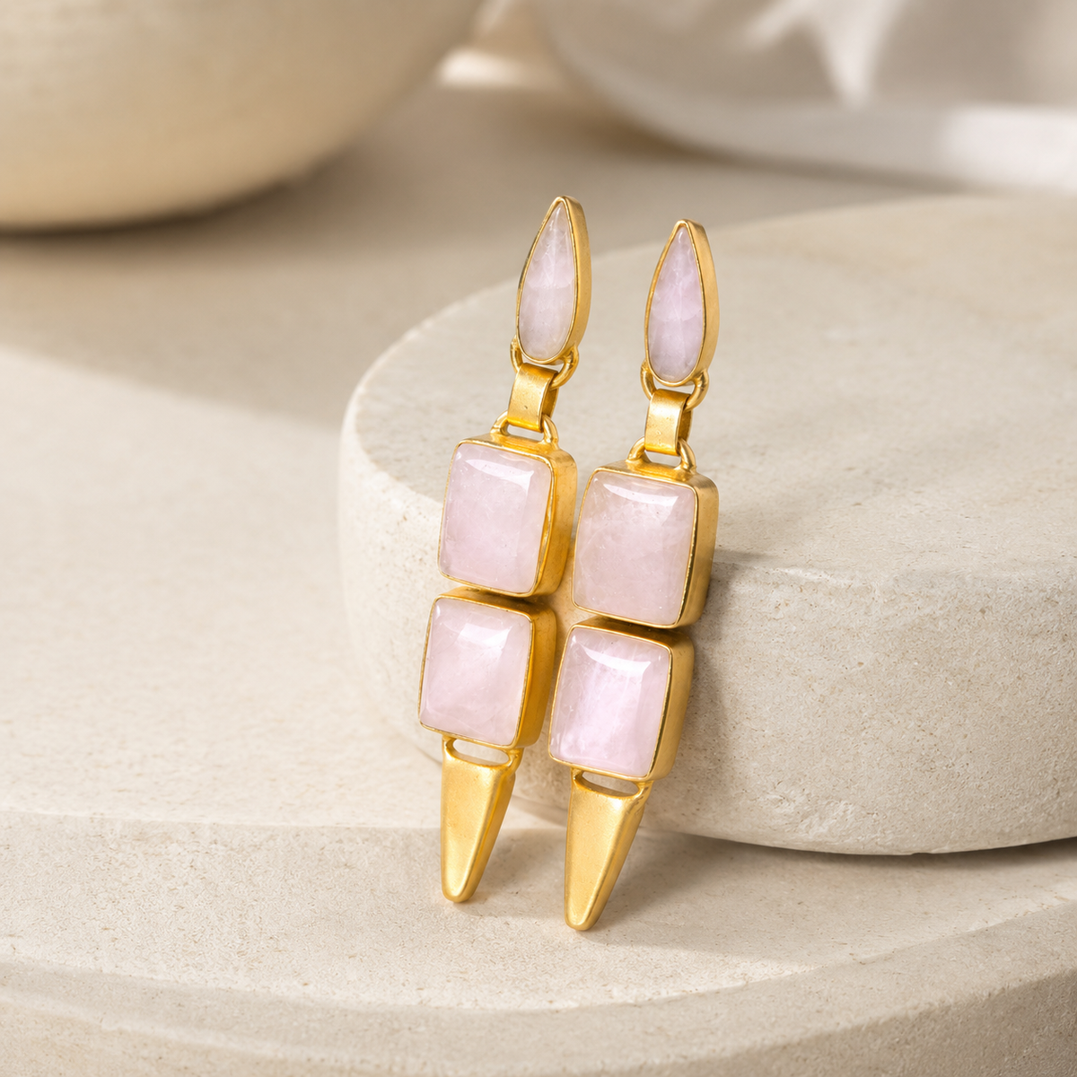 Angle view of geometric drop earrings with pink stones and gold-plated edges.