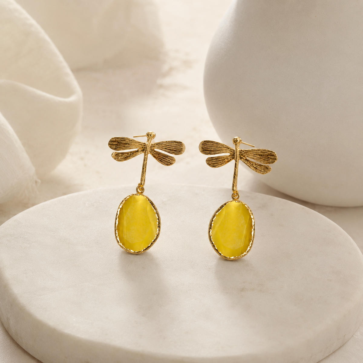 Gold dragonfly earrings with mustard-toned drops on a white background.