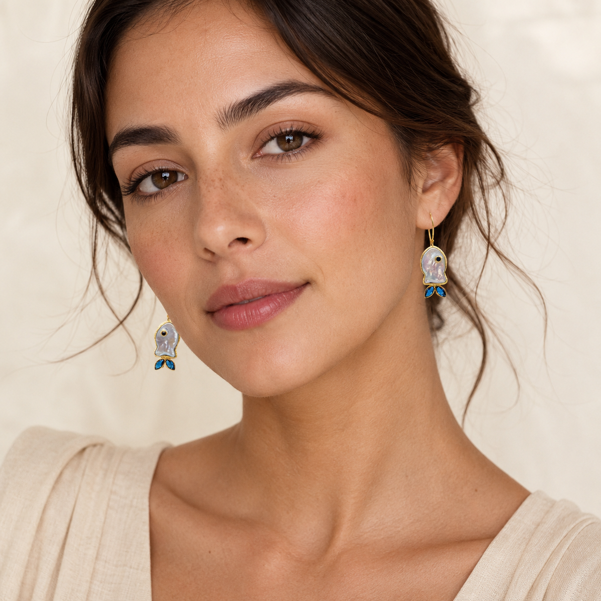 Mother-of-pearl fish earrings with blue CZ accents shown in a polished gold-plated style.