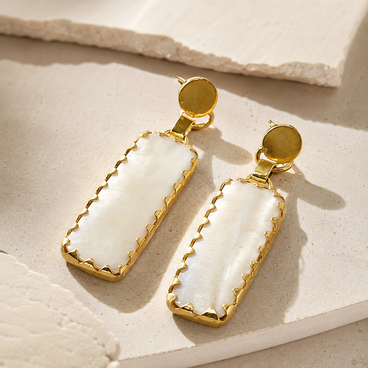 Angle view of gold-plated drop earrings with a round top and elongated rectangular drops.