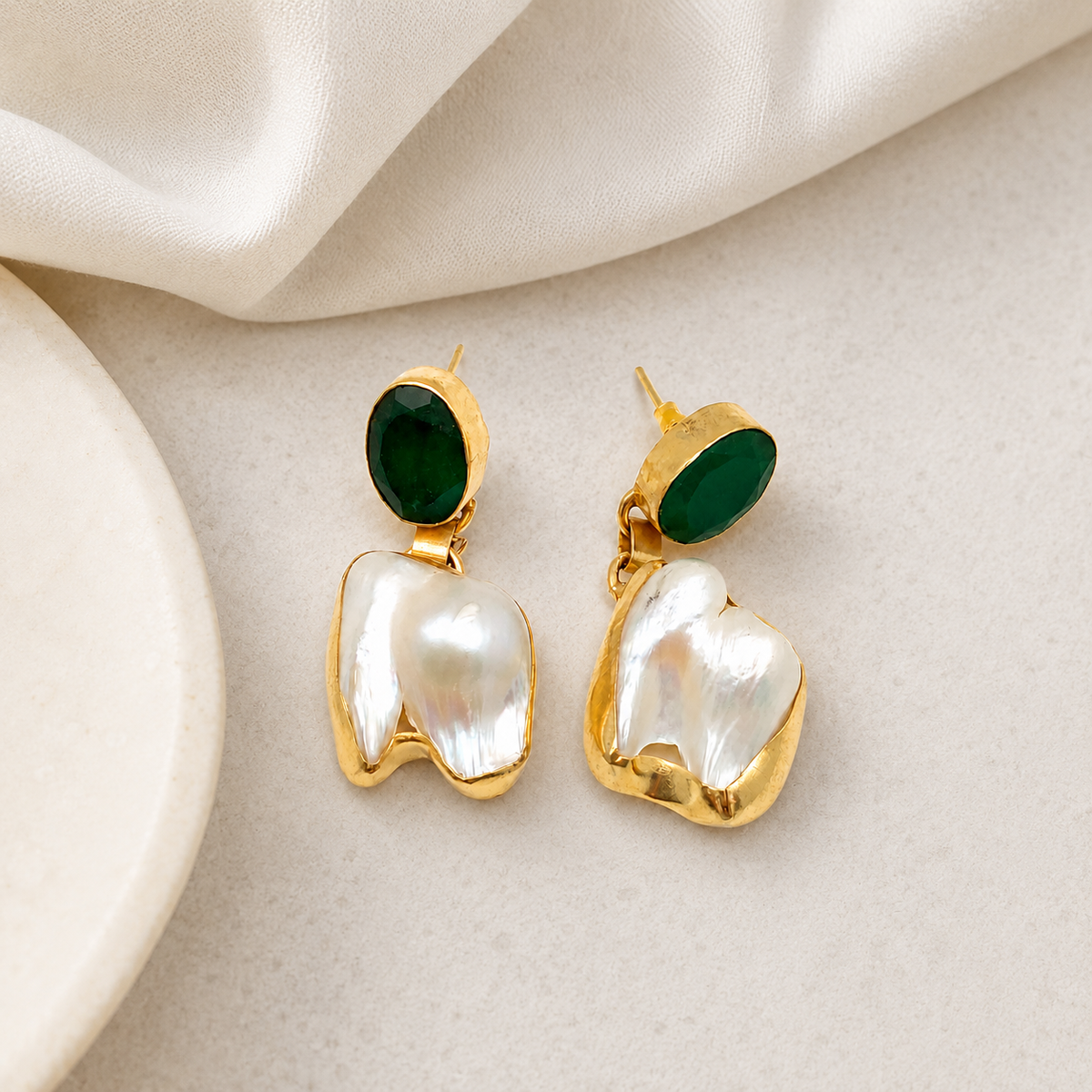 Gold-tone earrings with green oval stones and baroque pearl drops on a white background.