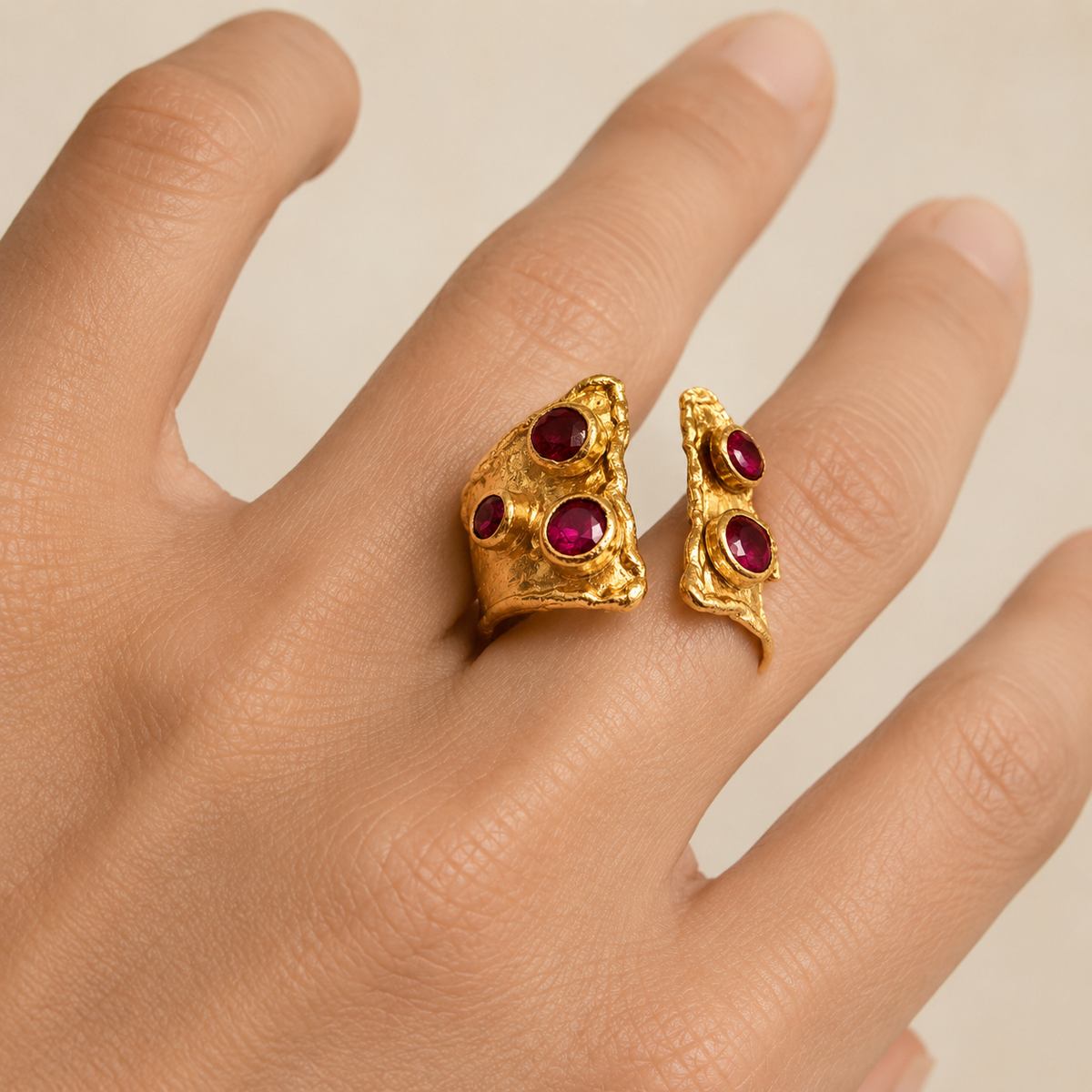Gold-plated open cuff ring with ruby pink stone accents shown on a white background.