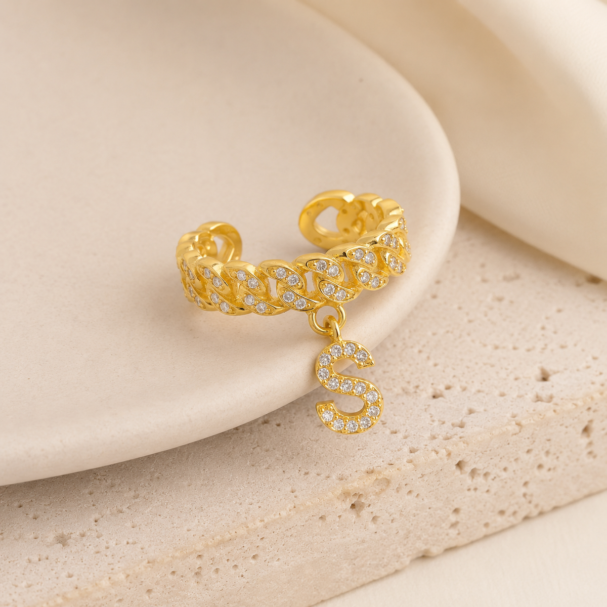 Angled view of a gold-tone cuff ring with sparkling CZ details and an initial pendant.