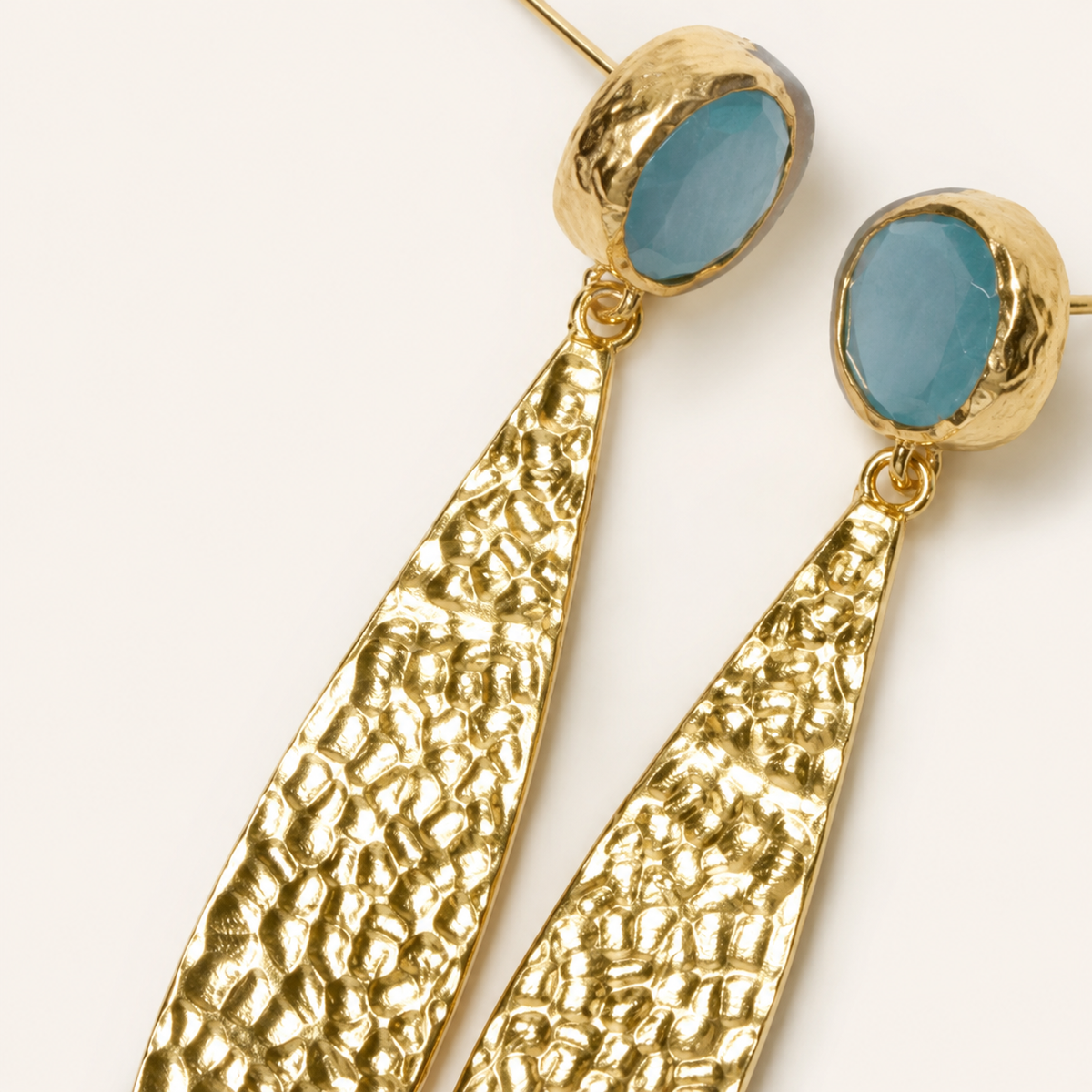 Close-up of hammered gold-plated drop earrings with textured detailing and blue oval tops.