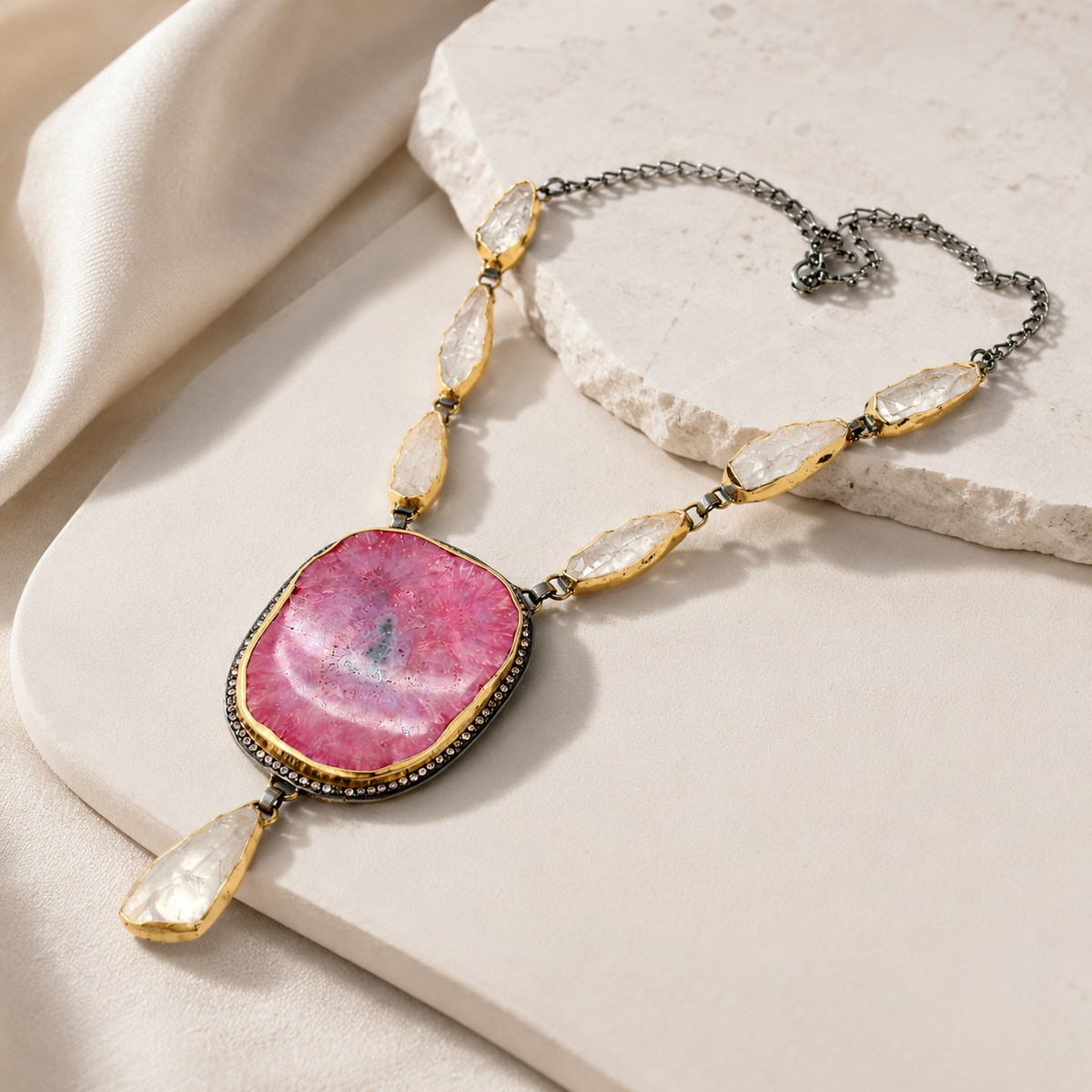 Angled view of the pink solar stone teardrop necklace with gold-tone details.