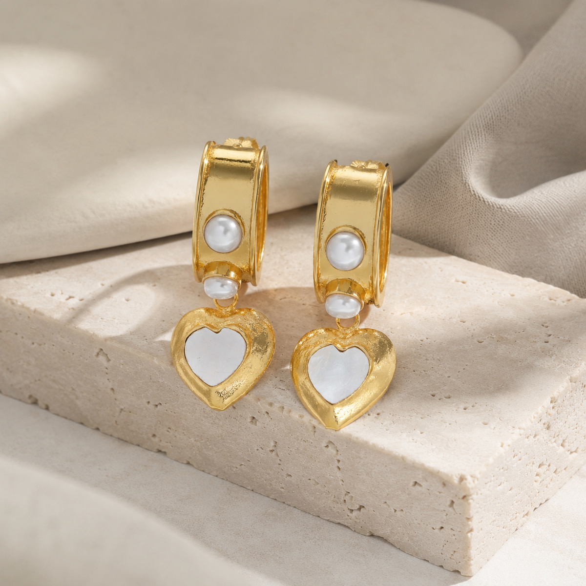 Angled view of gold-plated drop earrings with mother of pearl heart charms.