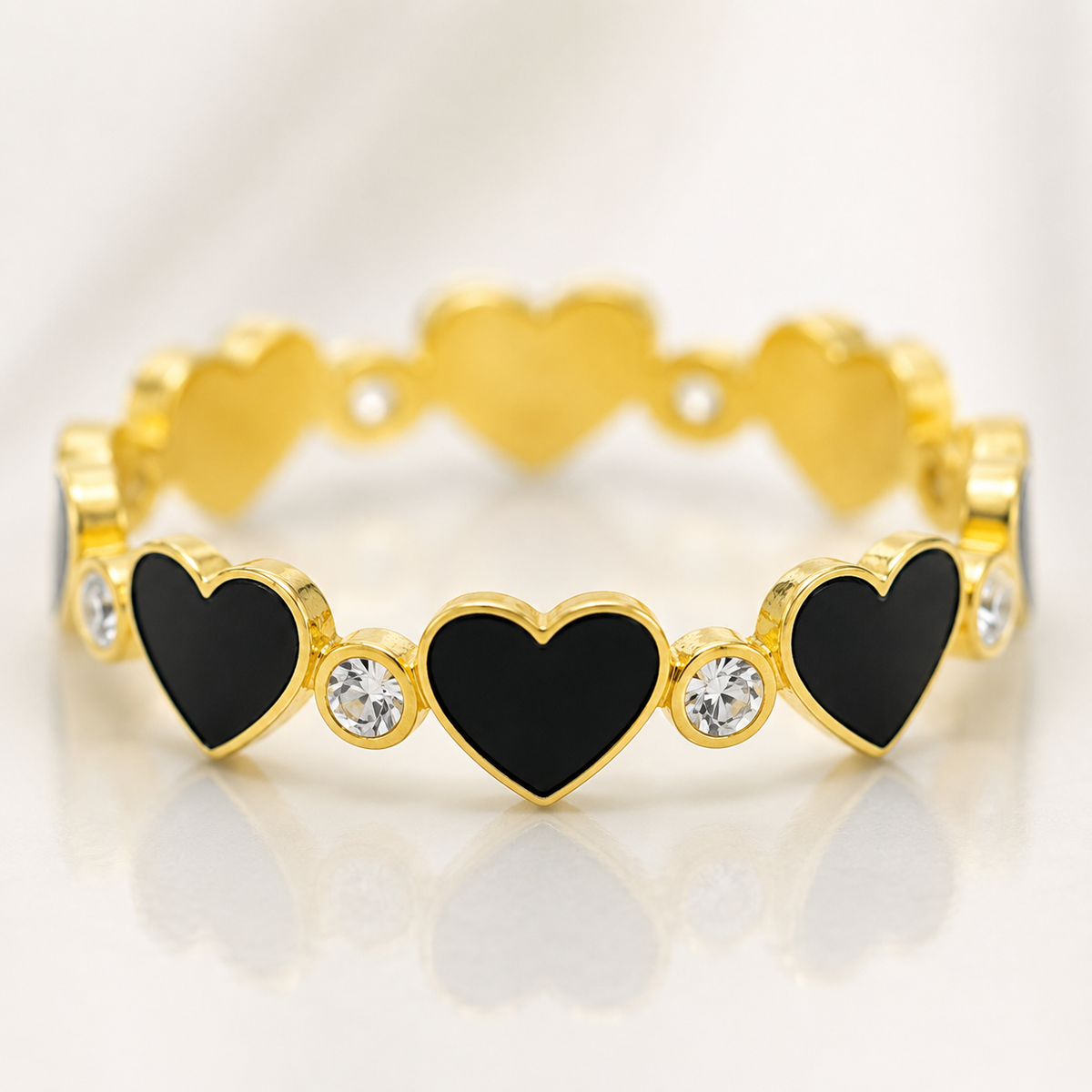 Close view of a gold-tone heart ring with black enamel-like accents and CZ stones.