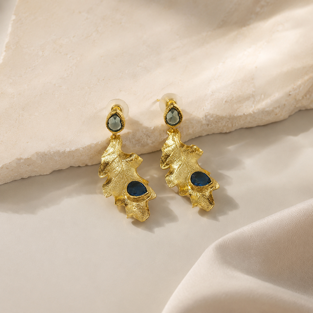 Gold plated drop earrings with leaf-shaped pendants and blue stones.