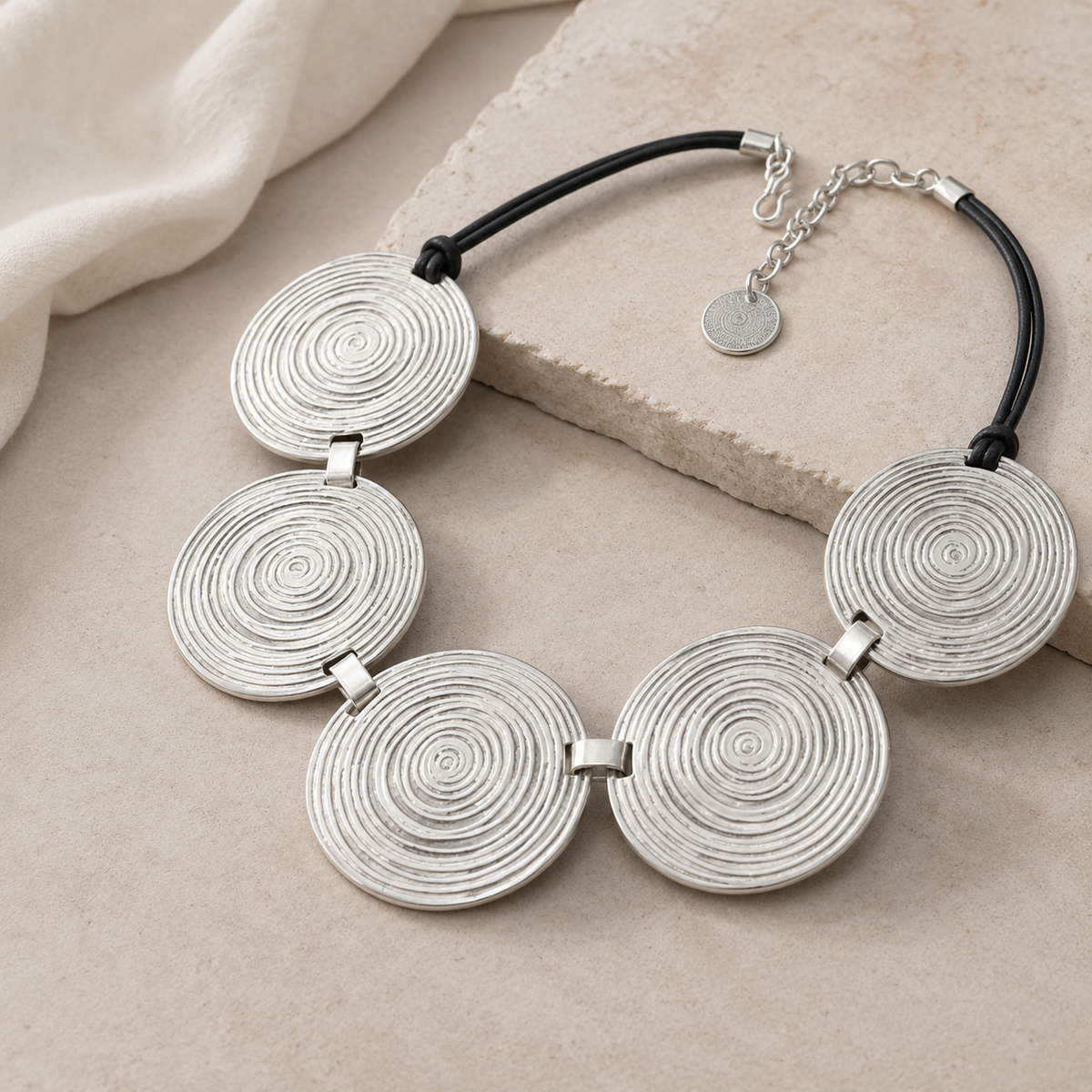 Angled view of a silver necklace with spiral disc pendants and black cord detail.