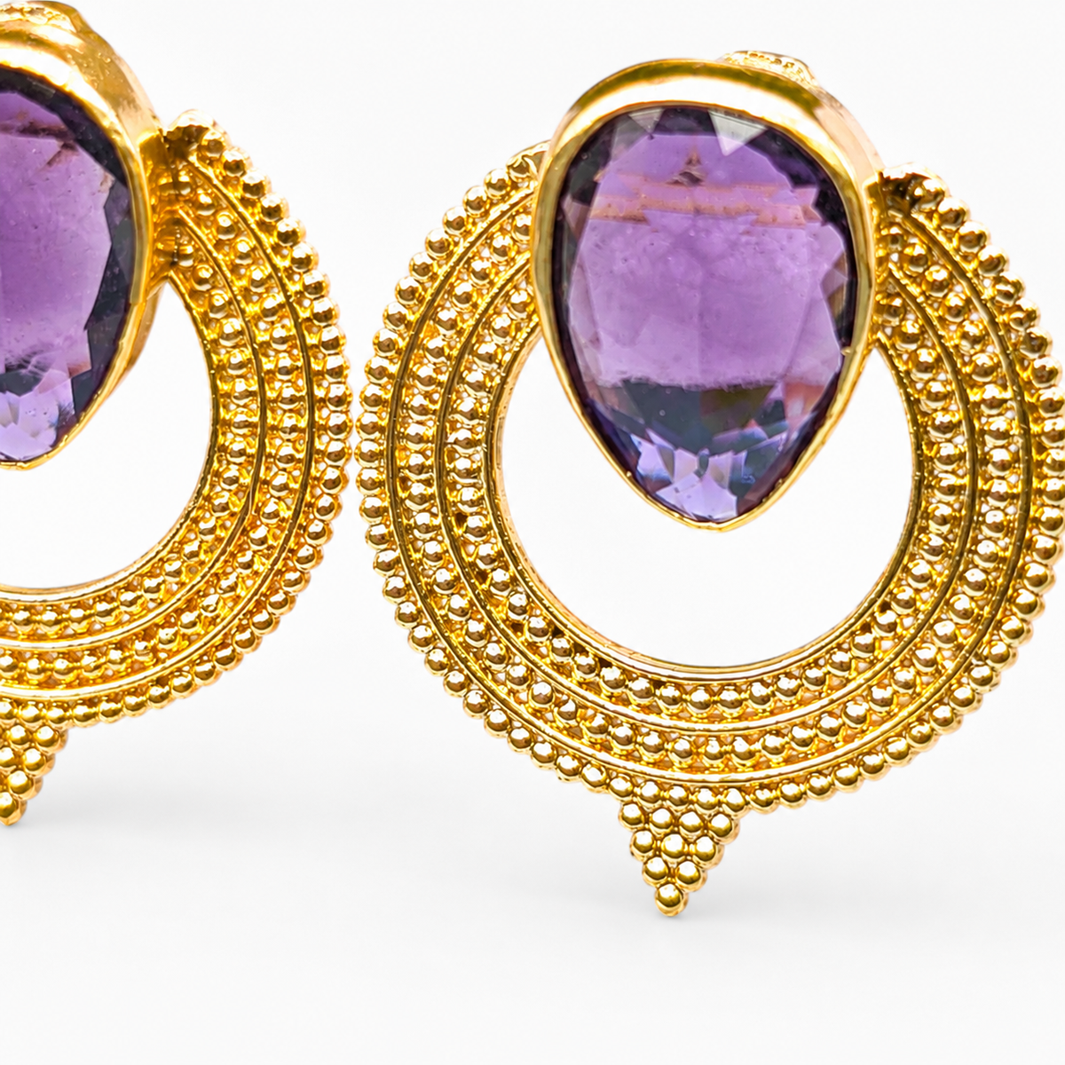 Close view of purple CZ stones set in gold-plated circular earrings.