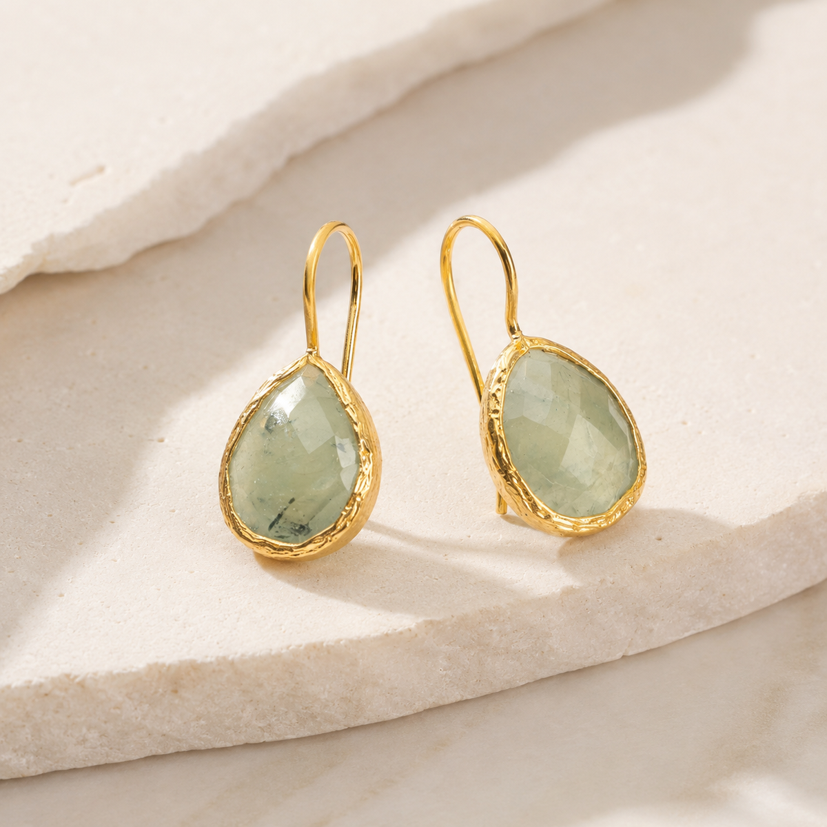 Angle view of gold-plated drop earrings with green teardrop stones.