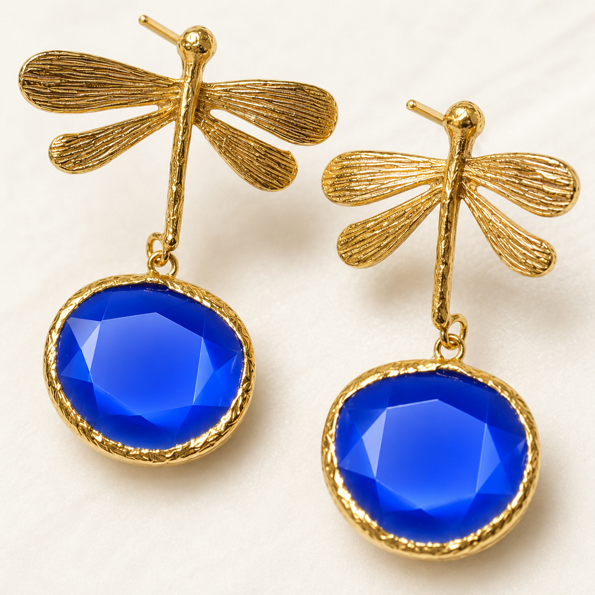 Close view of textured gold-plated dragonfly earrings and blue stones.