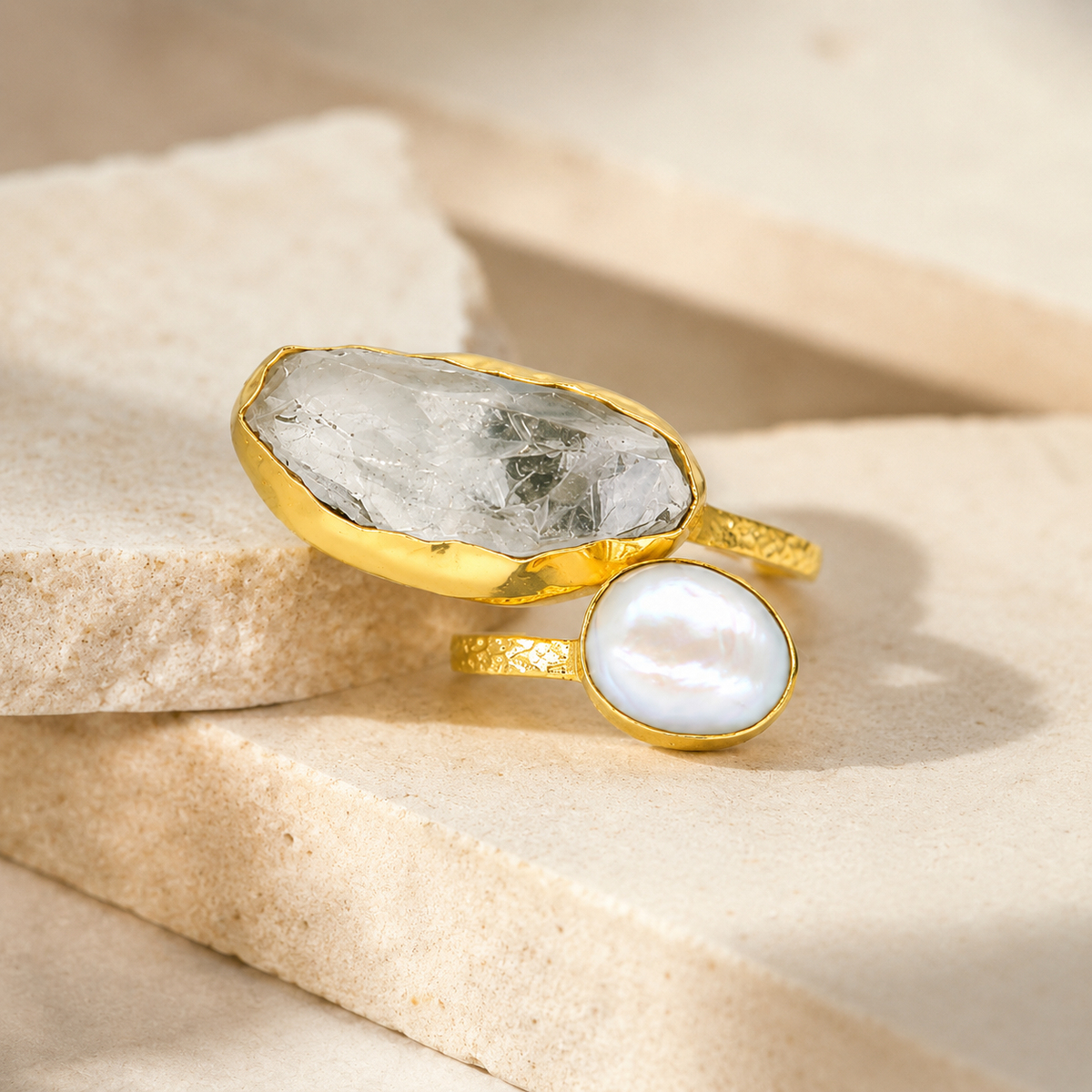 Angled view of a gold-plated ring with clear quartz and pearl-like stones.