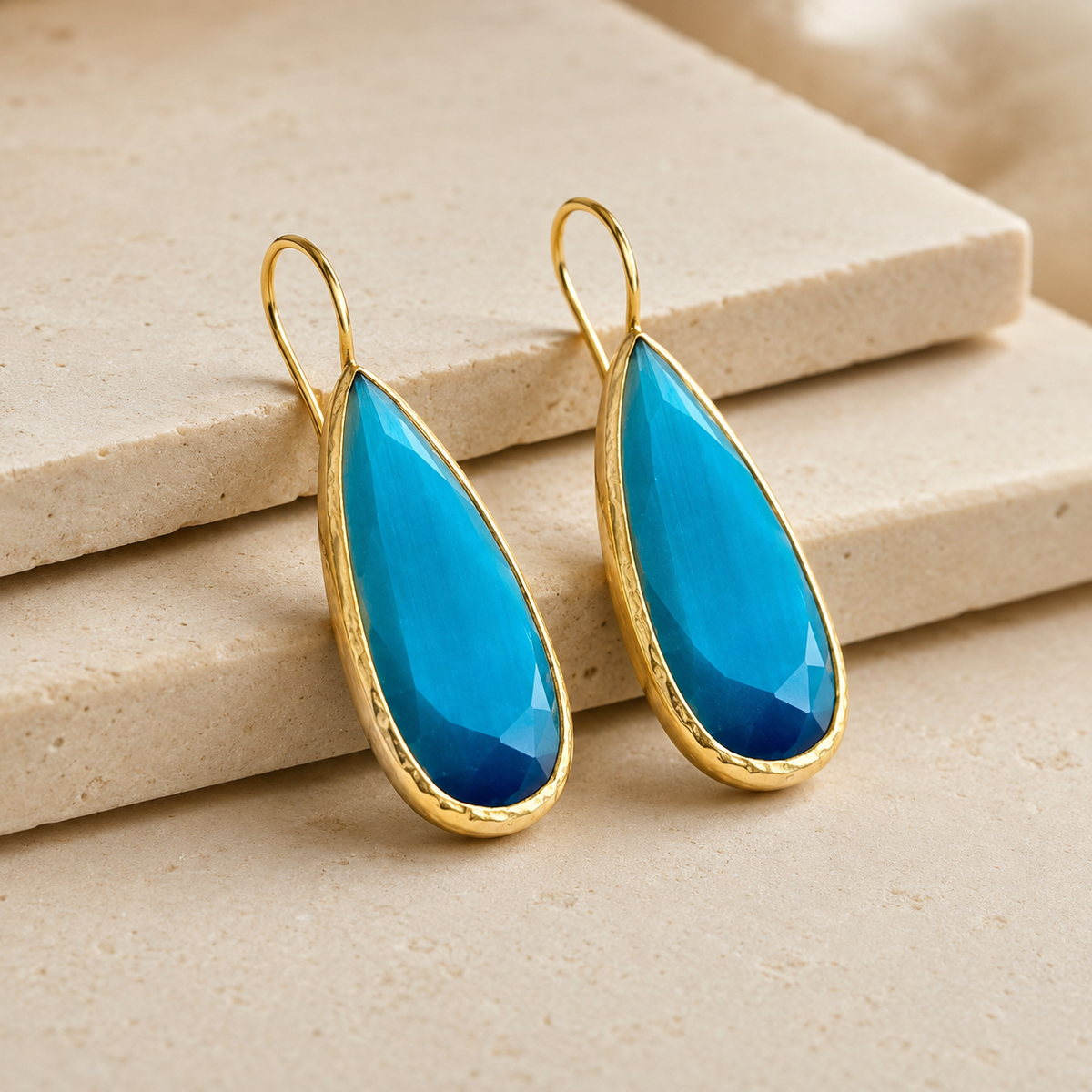 Angle view of ocean blue teardrop earrings with gold-plated brass framing.