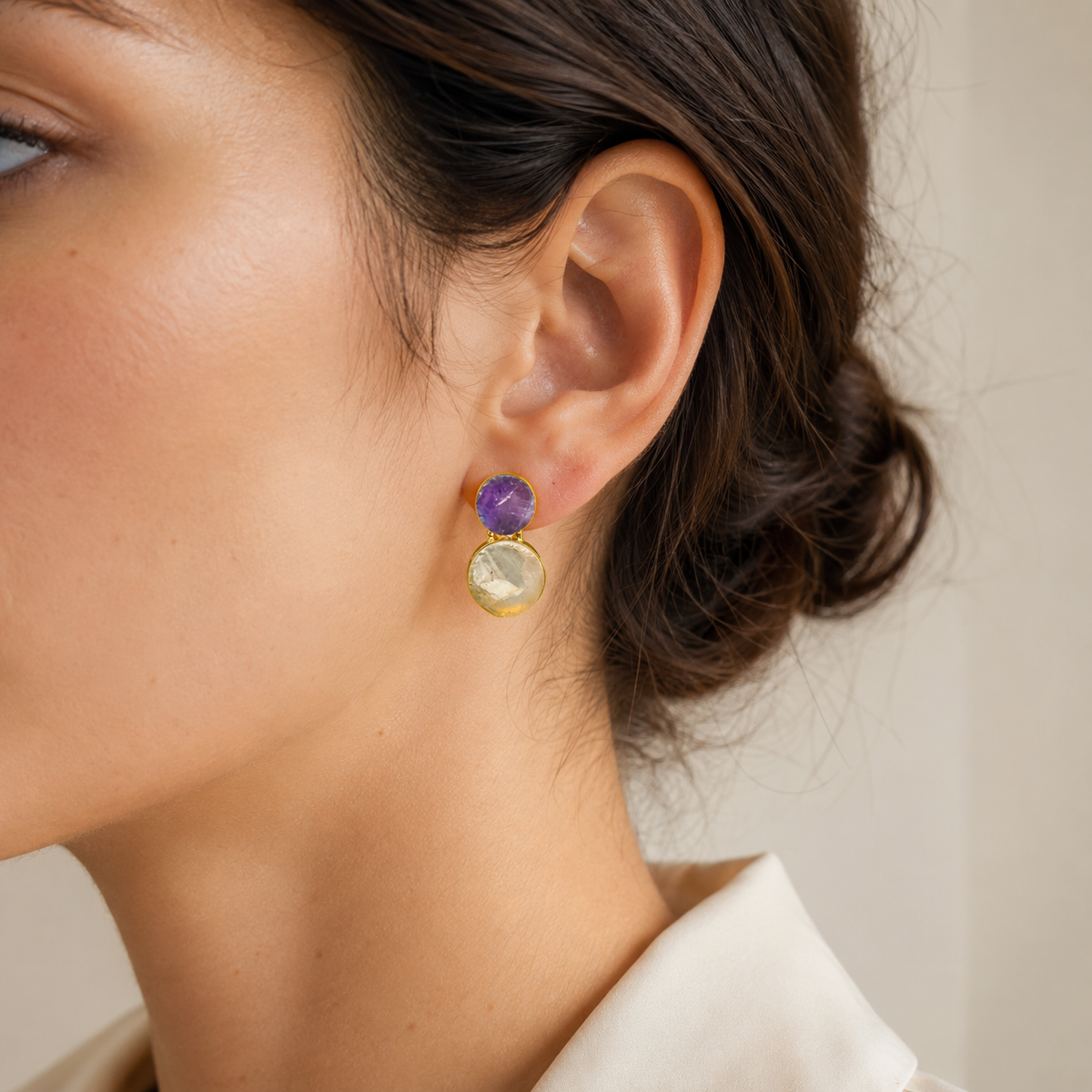 Close view of drop earrings with purple amethyst and clear quartz stones and a gold-plated finish.