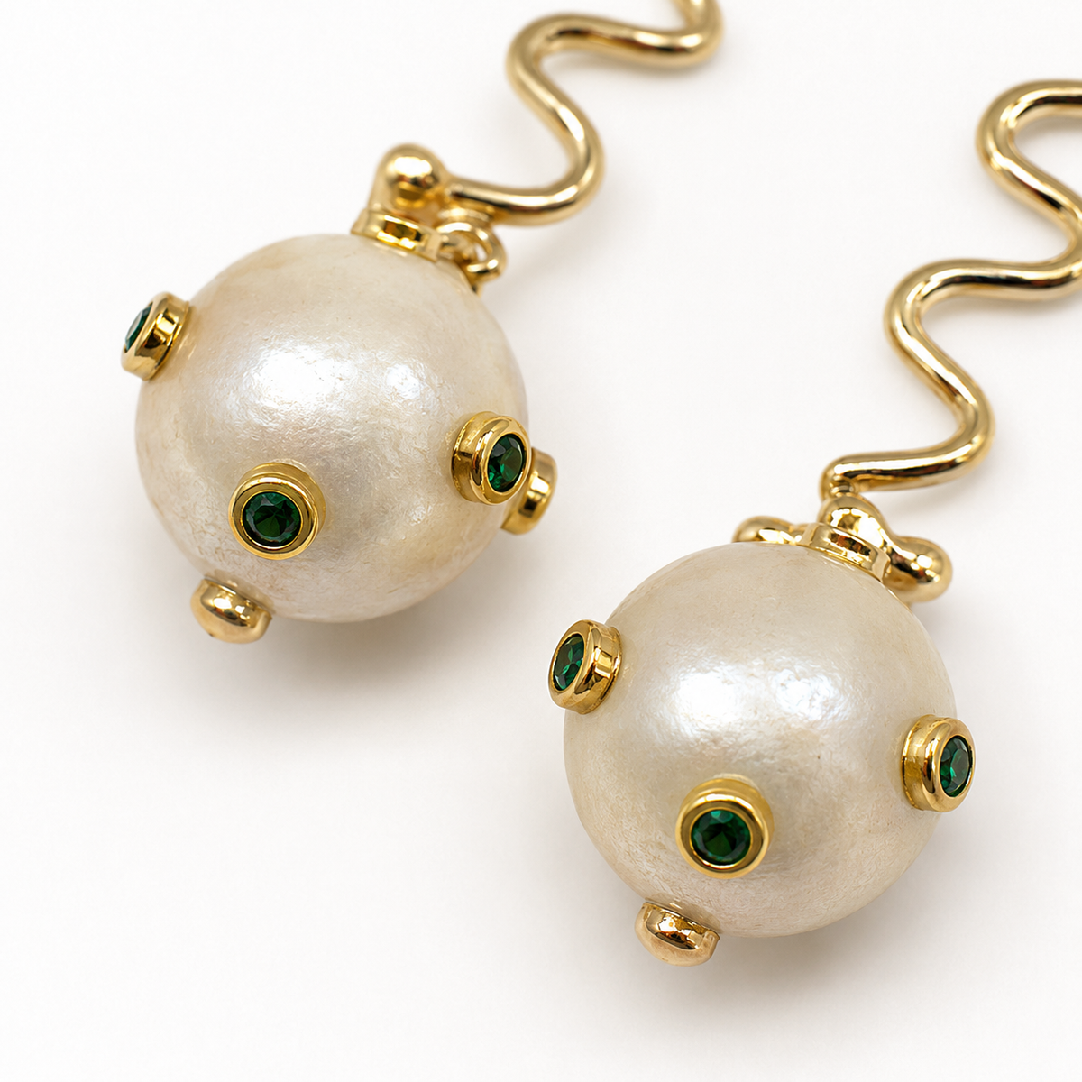 Close view of the pearl-like sphere and small green accent stones on the earrings.