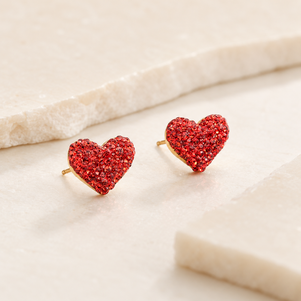 Angle view of red crystal heart stud earrings with a sparkling finish.