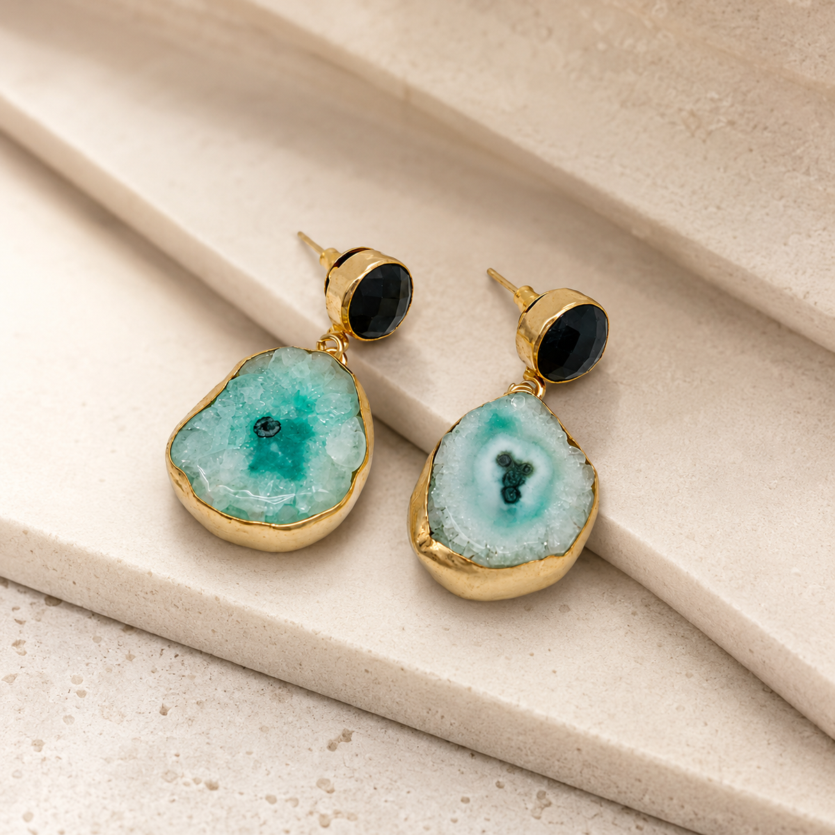 Angle view of gold-plated earrings with faceted black stone tops and rounded stone drops.