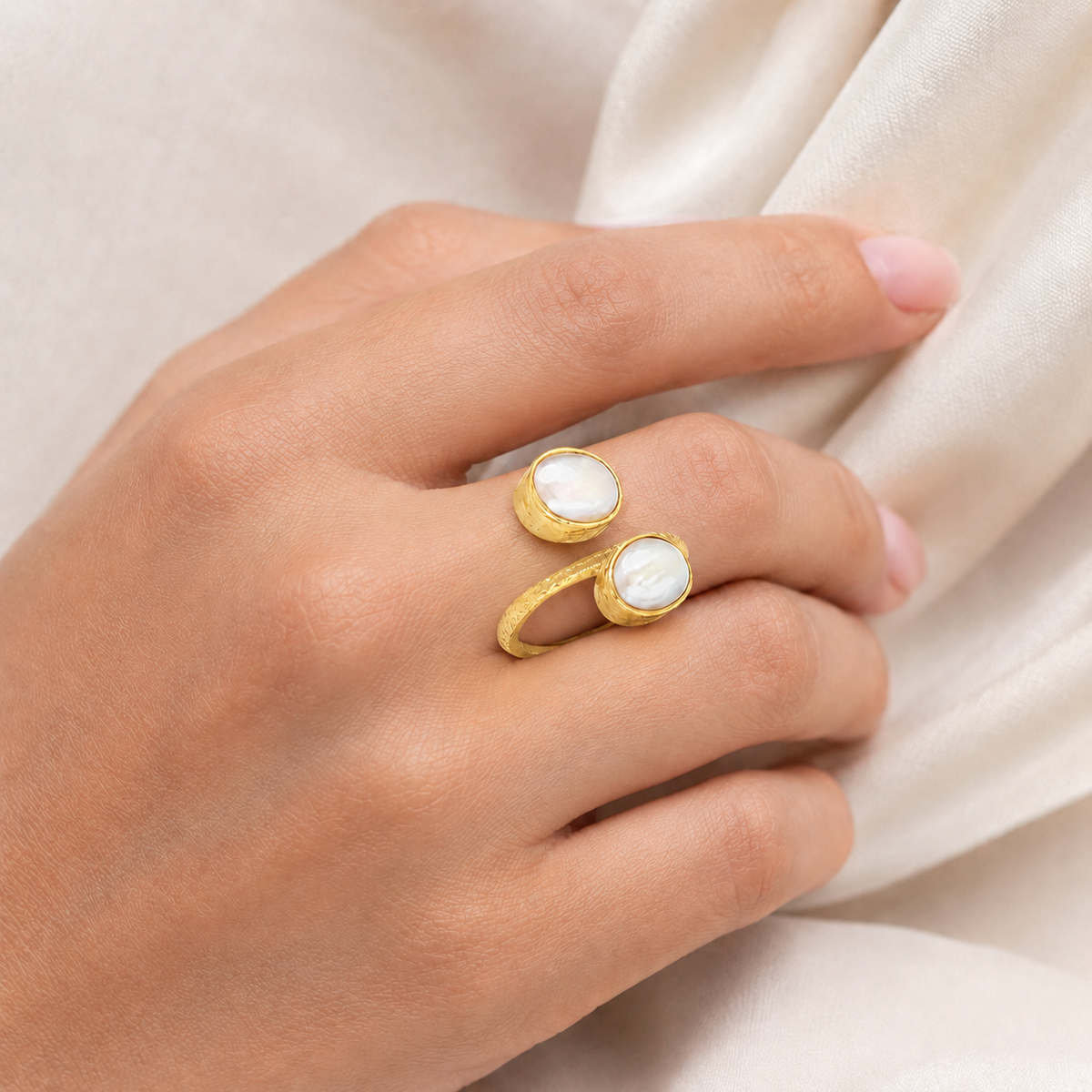 Gold-plated ring with two pearl-like stones on a hand.