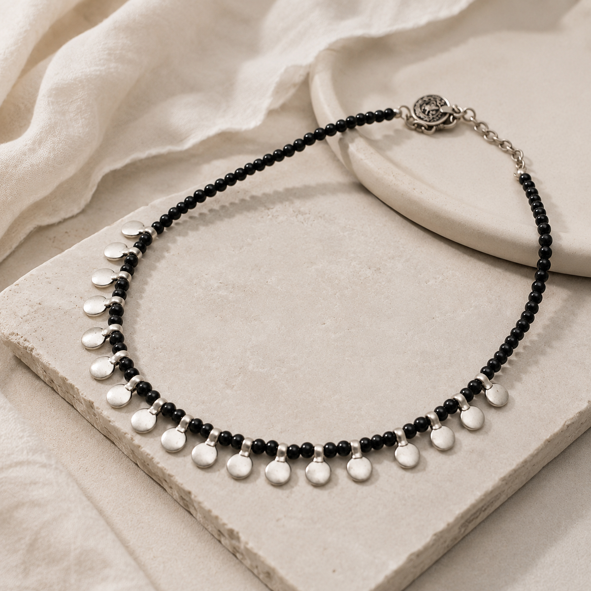 Angled view of a black bead necklace with silver disc accents.
