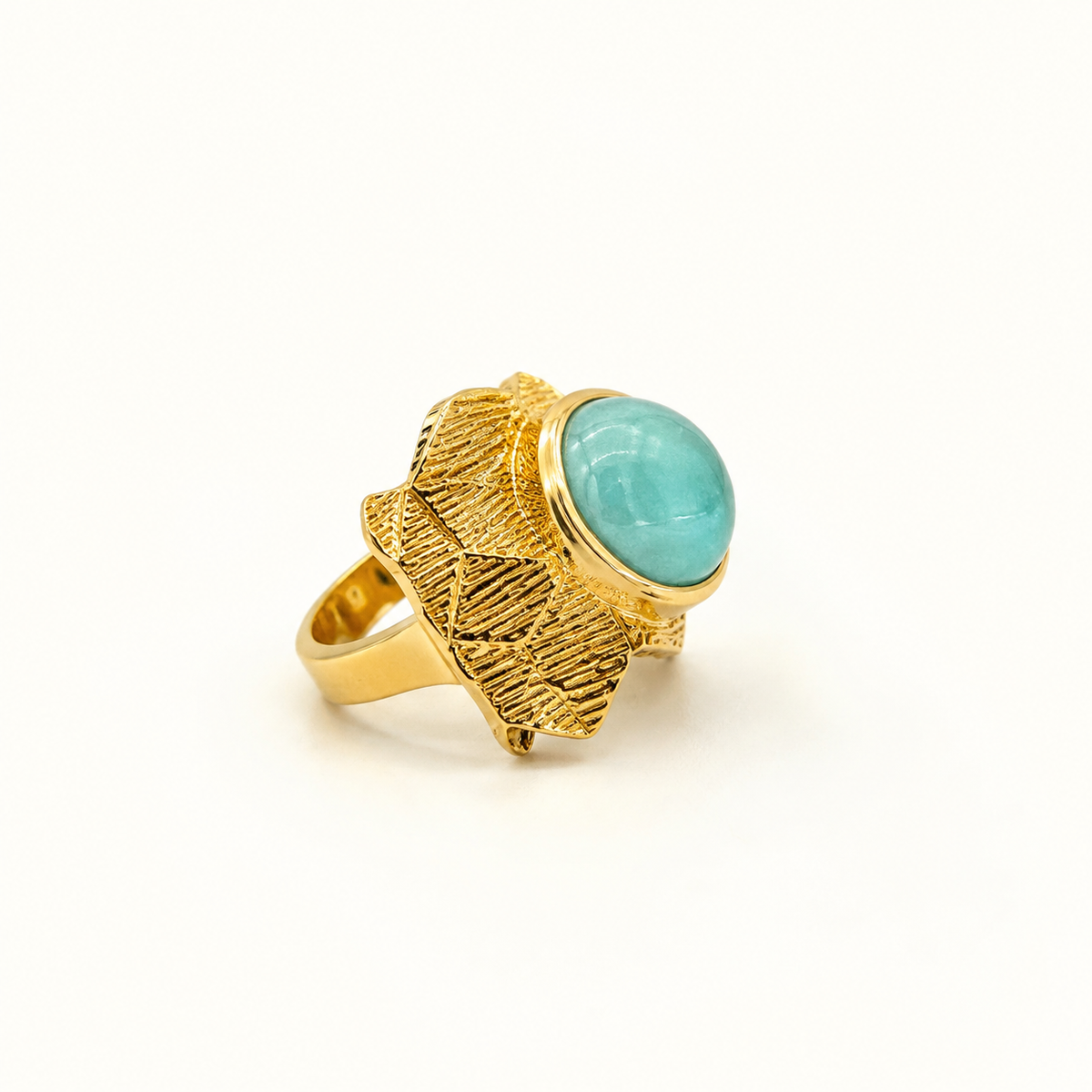 An angled view of a geometric gold-plated ring with a round aqua blue center.