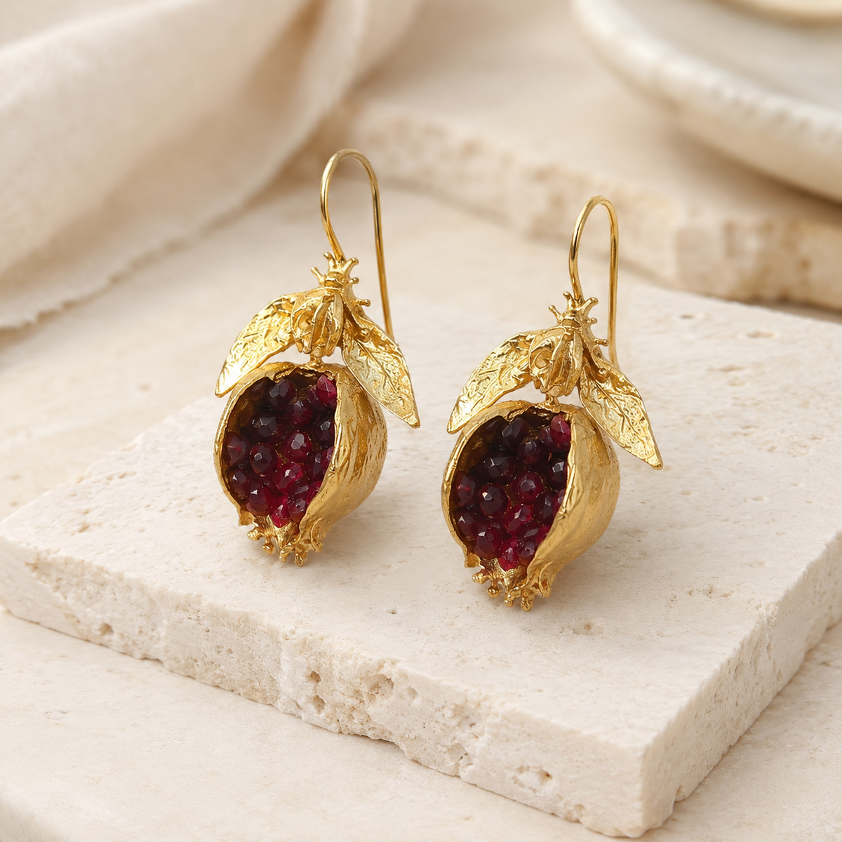 Angle view of gold-plated drop earrings with pomegranate-red stones.