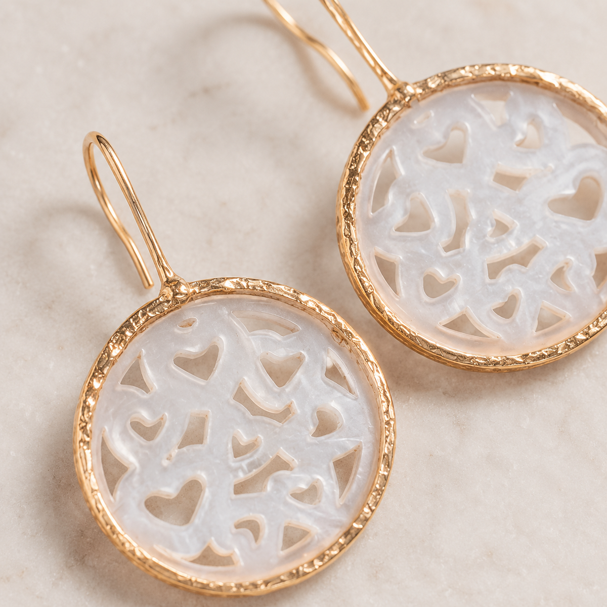 Close-up of gold-plated earrings with mother of pearl heart cutouts.