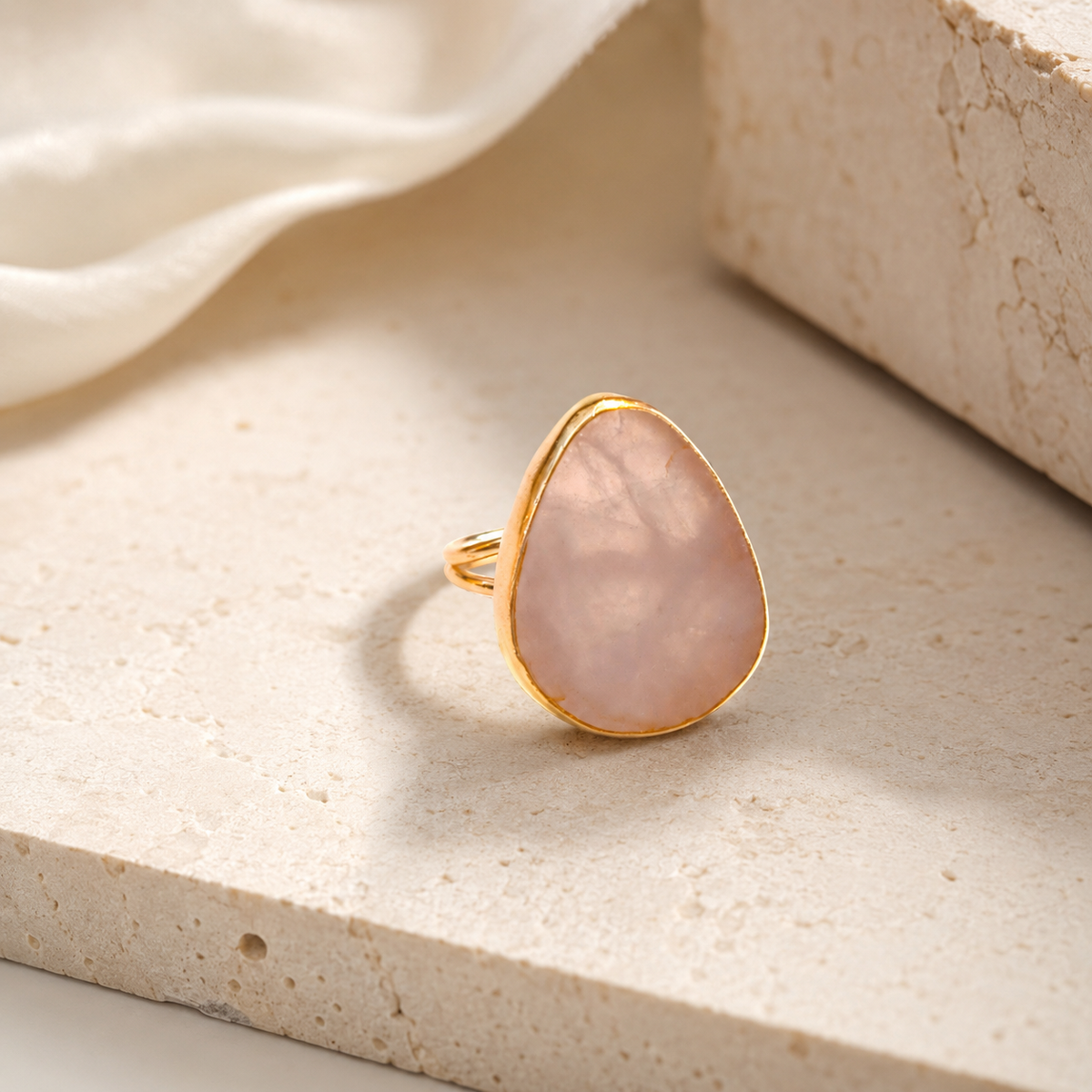 Angled view of a rose quartz teardrop statement ring in gold plating.