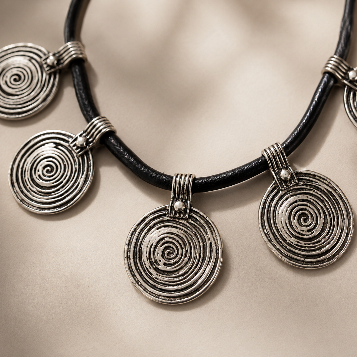 Close-up of spiral disc pendants on a black cord necklace.