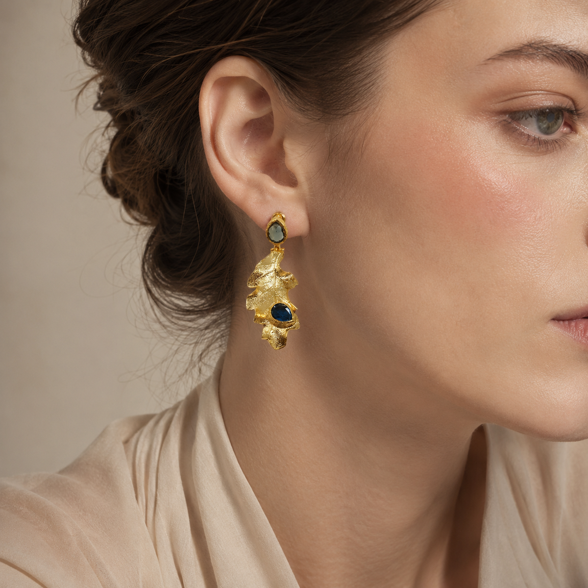 Pair of gold leaf drop earrings with blue stones on a white background.