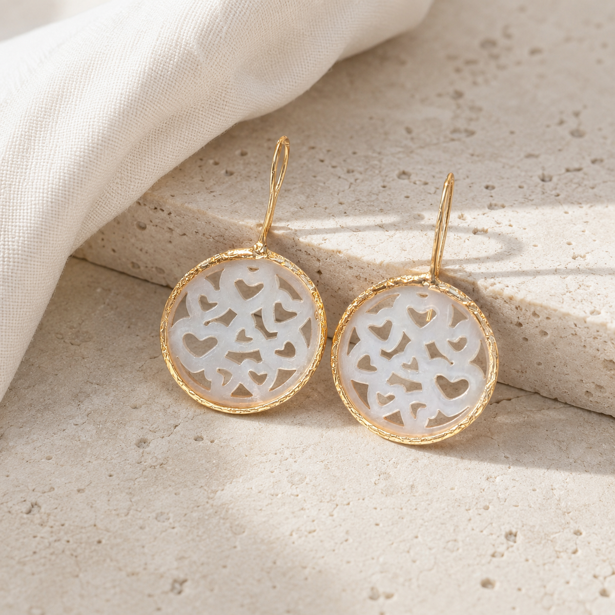 Gold-plated earrings with mother of pearl heart cutouts on a white background.