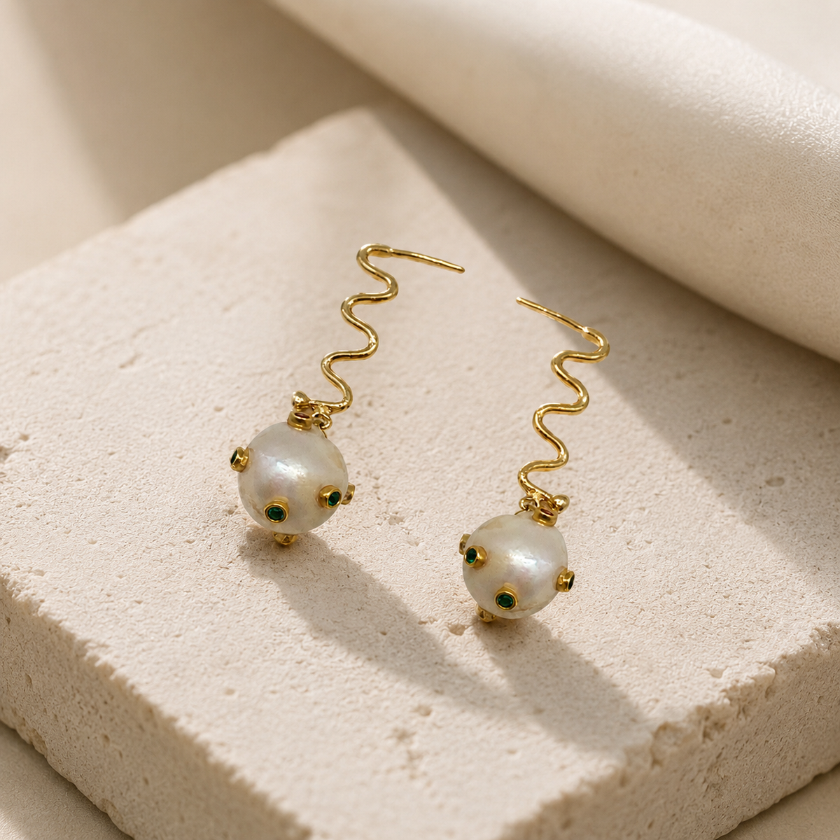 Angle view of gold-plated earrings with wavy hooks and pearl-like accents.