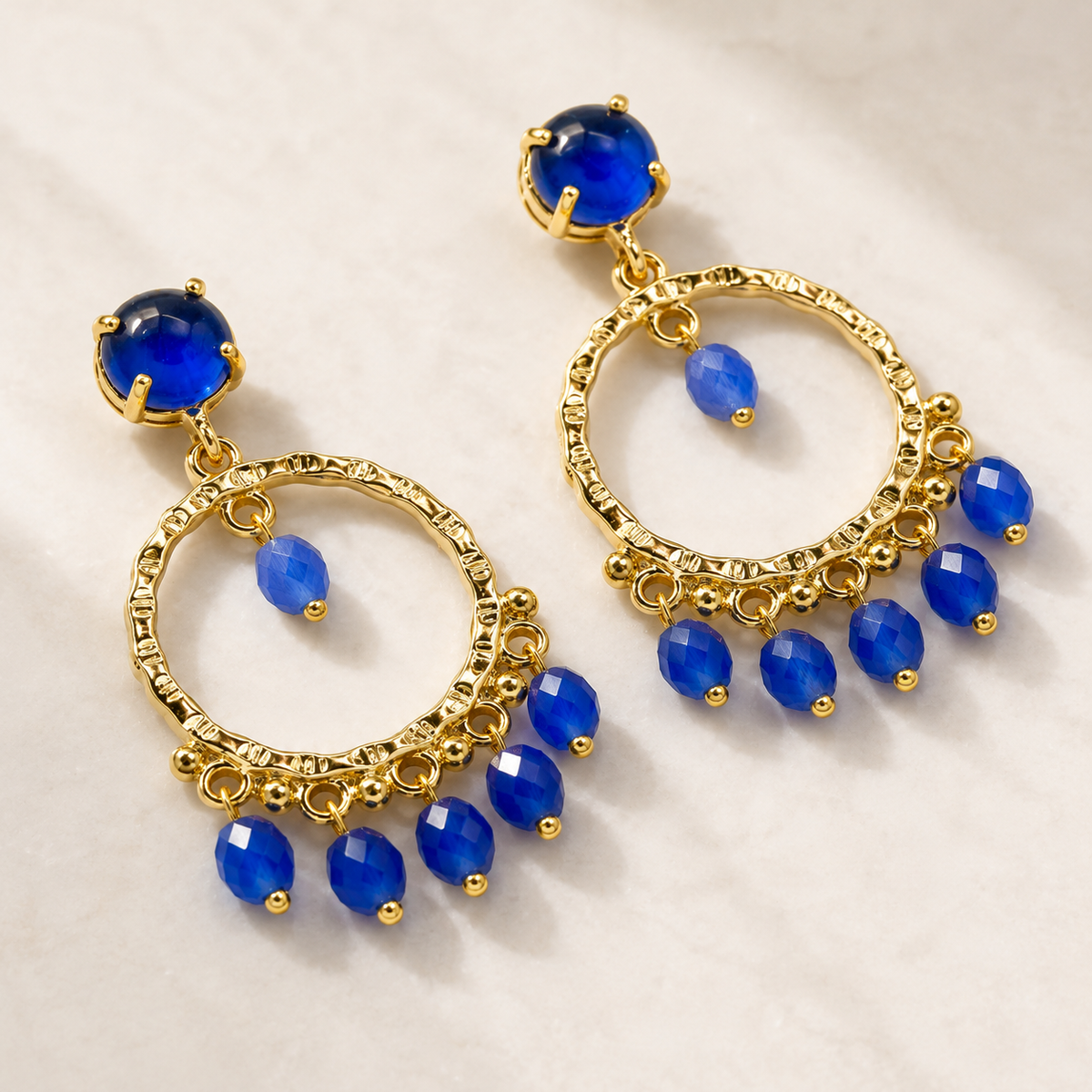 Angle view of gold-plated dangle earrings with bright blue stones.