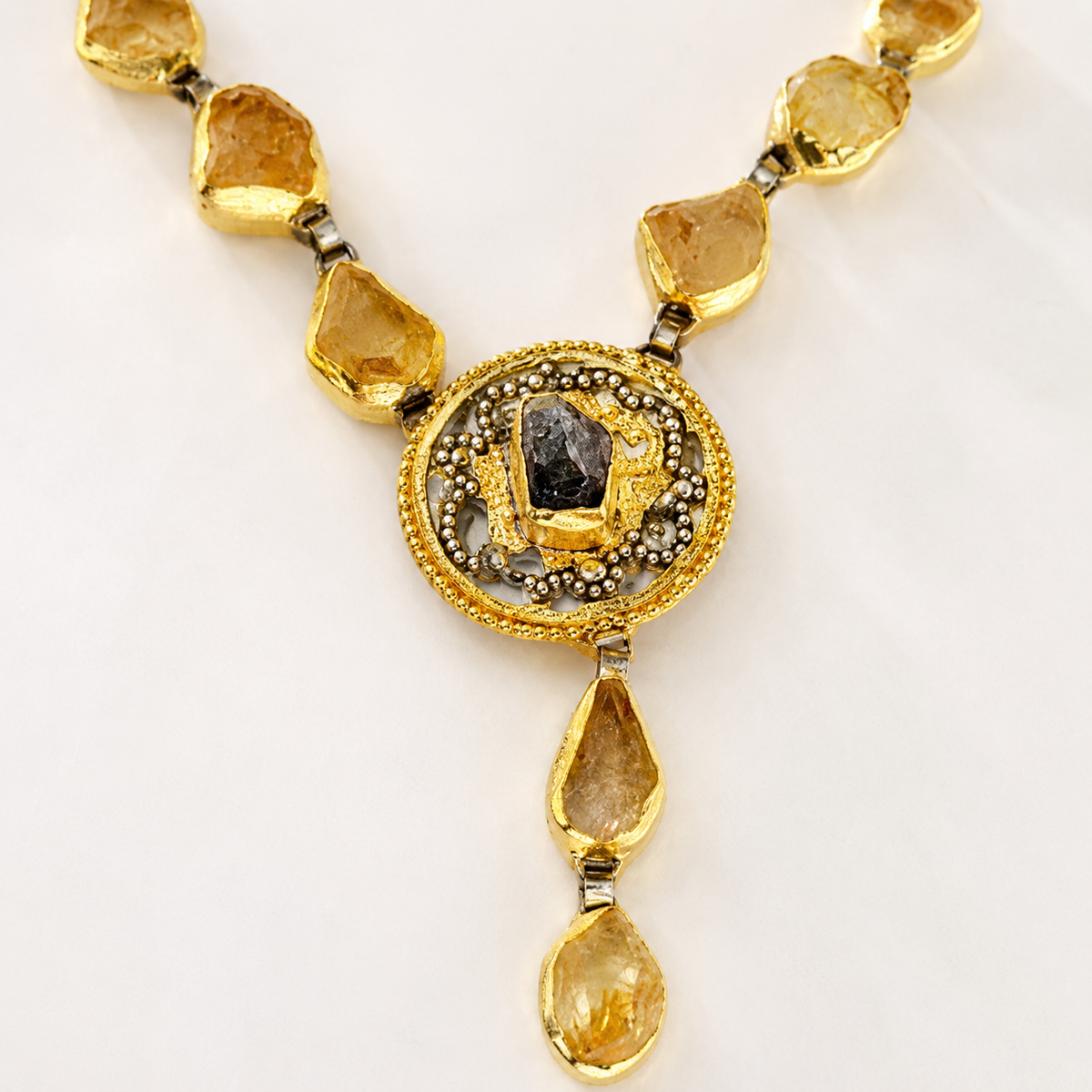 Close view of the medallion pendant and citrine-toned stone details on the necklace.