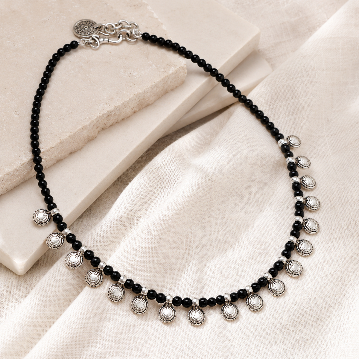 Angled view of a black bead necklace with round silver-tone charms.