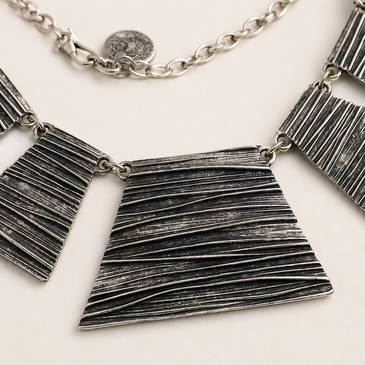 Close view of the necklace's textured silver-tone panels and chain.