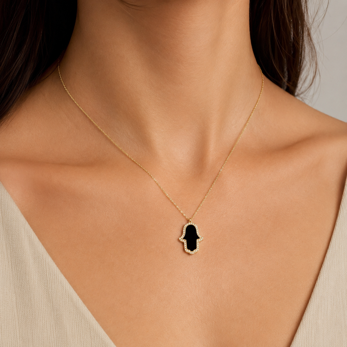 Gold-tone hamsa hand necklace with black enamel center and sparkling CZ details.
